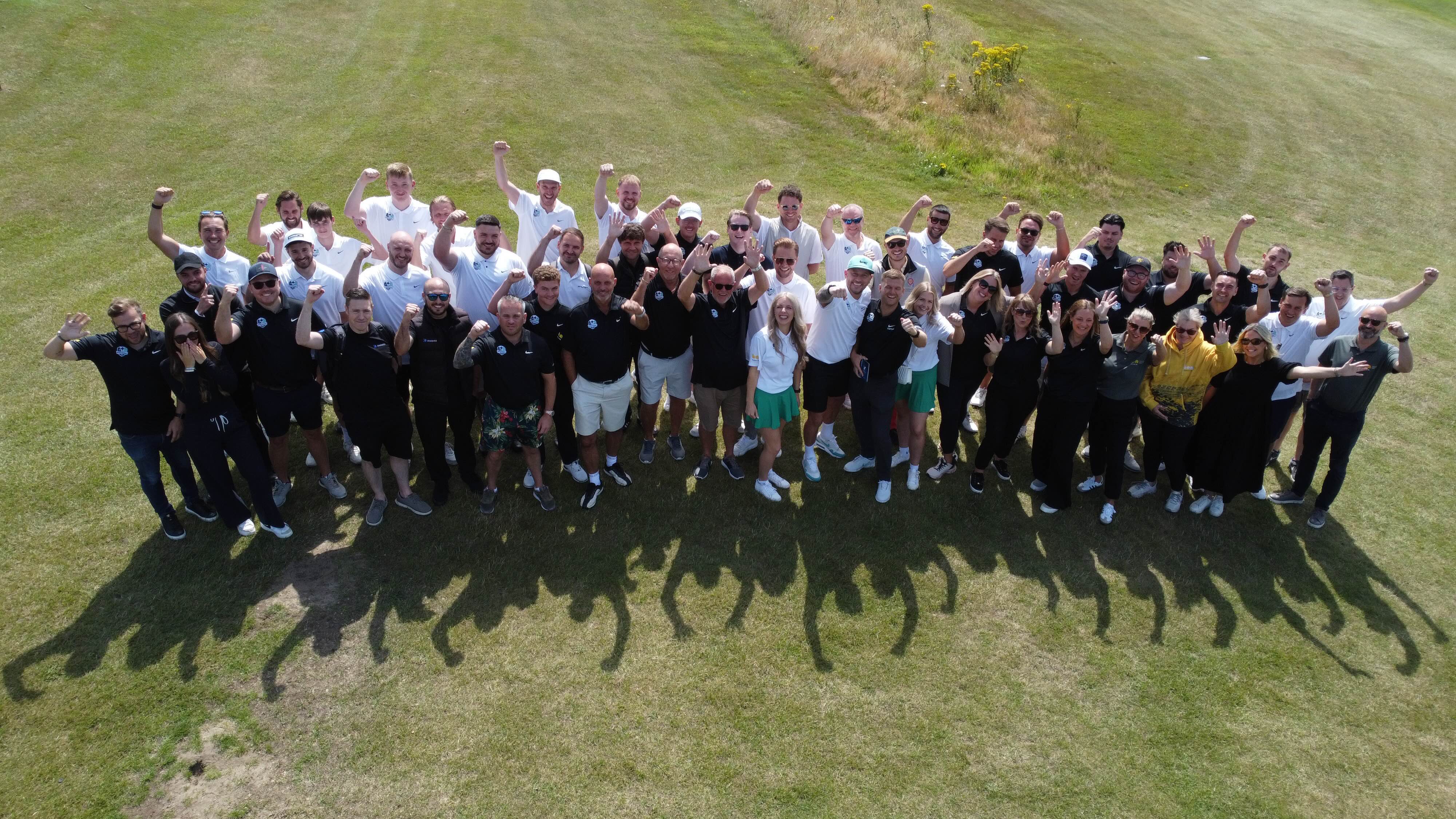 The group of golfers crowded together on the golf course cheering to the camera